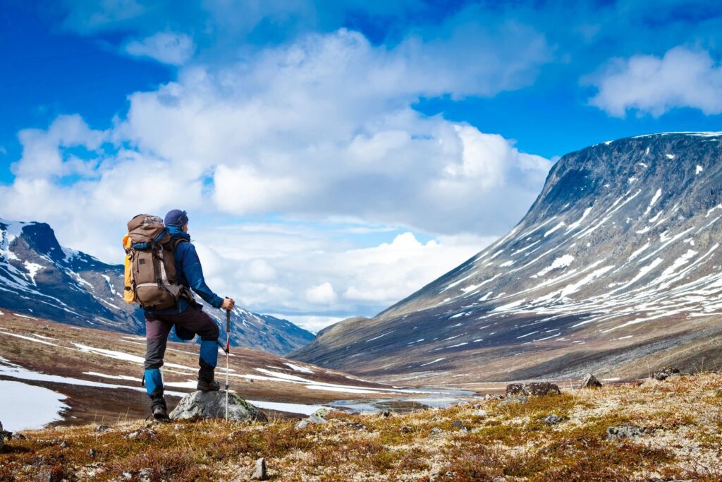 Man in sparsely snow capped mountains looking across the valley to the opportunity of climbing the largest mountain. 