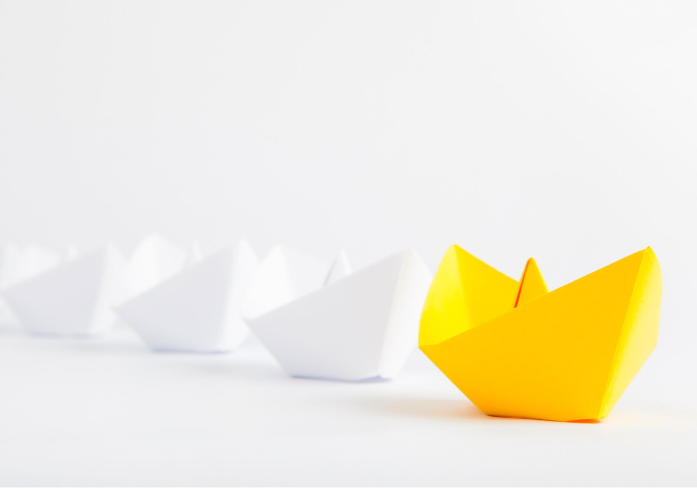 Yellow paper boat leading the path with five white boats behind